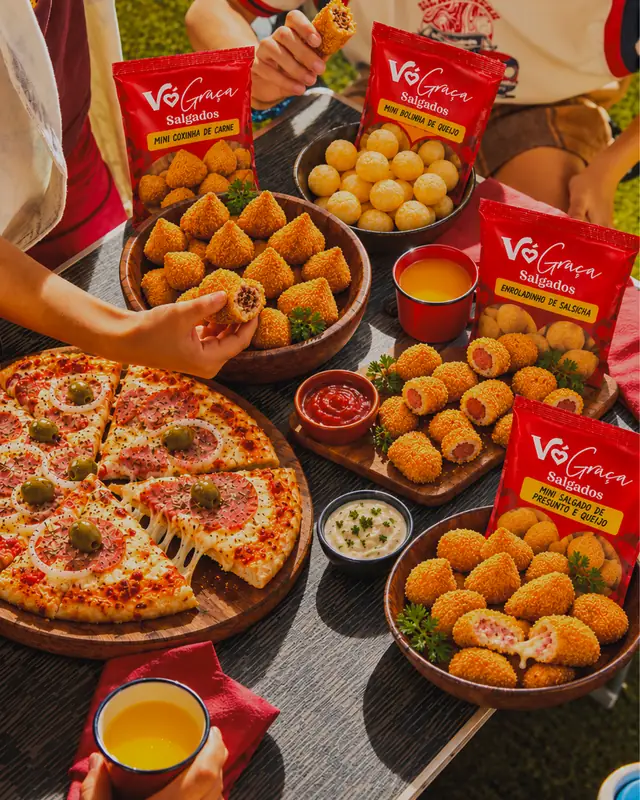 Mesa com salgados, pizza e pacotes Vó Graça